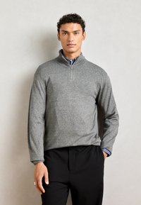 Gray zip-neck pullover knit sweater with long sleeves, featuring a textured fabric and contrasting blue collar underneath, paired with black trousers.