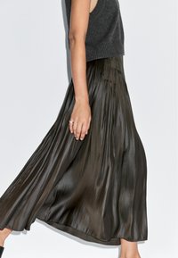 Pružná sukně v tmavě olivově zelené, vyrobená z lesklé a hladké látky, s vertikálními sklady a splývavým designem.