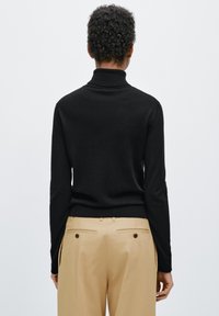 Czarny golf wykonany z miękkiej tkaniny, dopasowany krój, prążkowany kołnierz i mankiety. W zestawieniu z beżowymi, wysokim stanem spodniami.