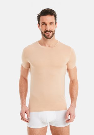 Slightly fitted nude short-sleeve T-shirt made of stretchy fabric, featuring a round neckline and smooth texture, worn with white shorts.