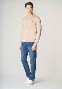 Maglione a maglia beige con scollatura rotonda, vestibilità slim. Abbinato a jeans blu e sneakers bianche. Presenta un piccolo logo sul maglione.