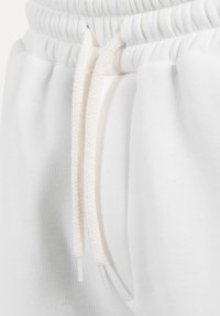 Bílé tepláky se stahovací šňůrkou v pase s pletenou texturou a průhlednými plastovými konci, vyrobené z měkkého bavlněného materiálu.