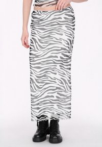 Áttetsző fekete-fehér zebra mintás maxi szoknya fodros szegéllyel, fekete bakancsokkal viselve. Sima textúra és testhezálló kialakítás.