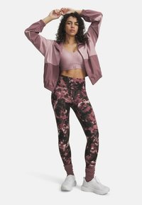 Athletic outfit featuring a pink cropped jacket, matching sports bra, and high-waisted leggings with a dark floral pattern; white sneakers.