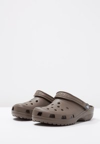 Bruna Crocs-träskor i lätt skum, med perforeringar för ventilation, rund tå och en stödjande hälrem.
