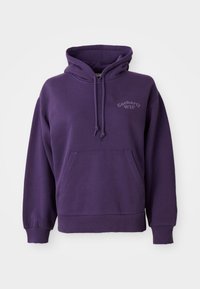Violetti puuvillahuppari, jossa on etutasku, nyöripäällinen ja vaalean violetilla "Carhartt WIP" -logo rinnassa. Pehmeä rakenne.