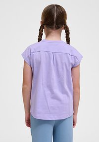 Lila Baumwoll-T-Shirt mit kurzen Ärmeln, mit einem Rückenfalten und abgerundetem Saum. Tragen mit hellblauen eng anliegenden Hosen.