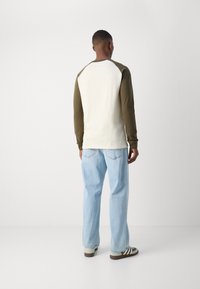 Pikend käised T-särk kreemjas kehaga ja oliivroheliste varrukatega, millel on mugav lõige ja ribatšiki kaelus, kombineeritud heleduse siniste teksadega.