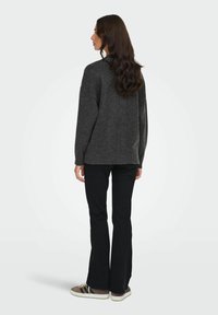 Maglione di lana grigio scuro con una vestibilità rilassata, maniche lunghe e retro leggermente corto. Abbinato a pantaloni svasati neri e sneakers.