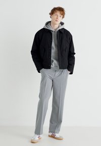 Black cropped jacket, gray hoodie, light gray trousers, and white sneakers with red stripes. Simple, casual design with soft textures.