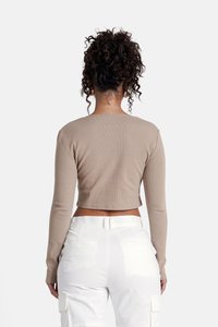 Beige-langärmliges geripptes Crop Top mit Rundhalsausschnitt. Auf Taillenhöhe abgeschlossen, kombiniert mit weißen Cargo-Hosen mit seitlichen Taschen.