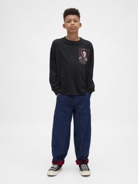 Tricou negru cu mâneci lungi, cu grafică imprimată pe piept, asortat cu blugi largi din denim albastru închis și pantofi sport negri cu talpă albă.