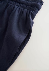 Pantaloni di cotone blu navy con vita elastica, che mostrano una texture liscia e dettaglio della tasca laterale, posizionati su uno sfondo chiaro.