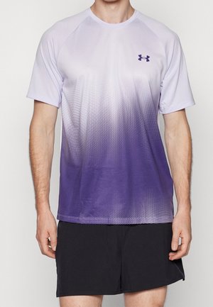 Homme portant un t-shirt de sport à manches courtes dégradé violet et blanc avec le logo Under Armour et un short de sport noir, debout les bras détendus.