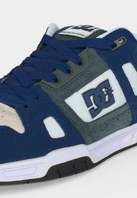 Μπλε, γκρι και άσπρο παπούτσι DC για σκέιτ με χοντρά κορδόνια, διάτρητα πάνελ σουέτ και λαστιχένια σόλα με μαύρες λεπτομέρειες πάτου.