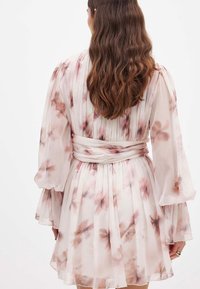 Krilo z rožnatim vzorcem, z naborki, narejeno iz lahkega materiala. Ima dolge rokave in vrvico v pasu, v mehkih rožnatih in bež tonih.