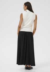 Hvid ærmeløs top med en mock collar, parret med en svævende sort maxiskørt. Glat tekstur, minimalistisk design og flade sorte sko synlige.