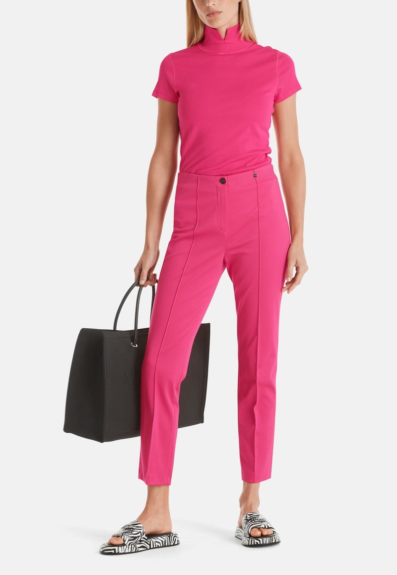 Haut fuchsia à manches courtes avec un col haut, associé à un pantalon fuchsia ajusté. Sac fourre-tout noir et sandales à glissière noir et blanc à motif zèbre.