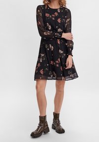 Vestido negro floral con largas mangas transparentes, puños fruncidos y una falda acampanada. Llevado con botas de combate oscuras y brillantes.