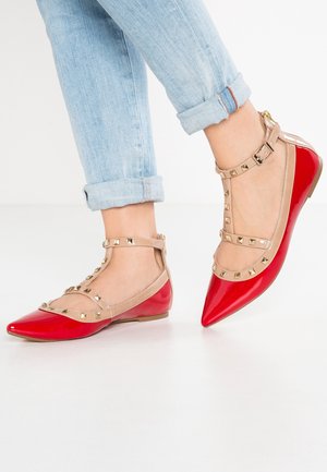 Red patent flats with a pointed toe and transparent beige straps featuring gold studs. Textured surface with a smooth finish.