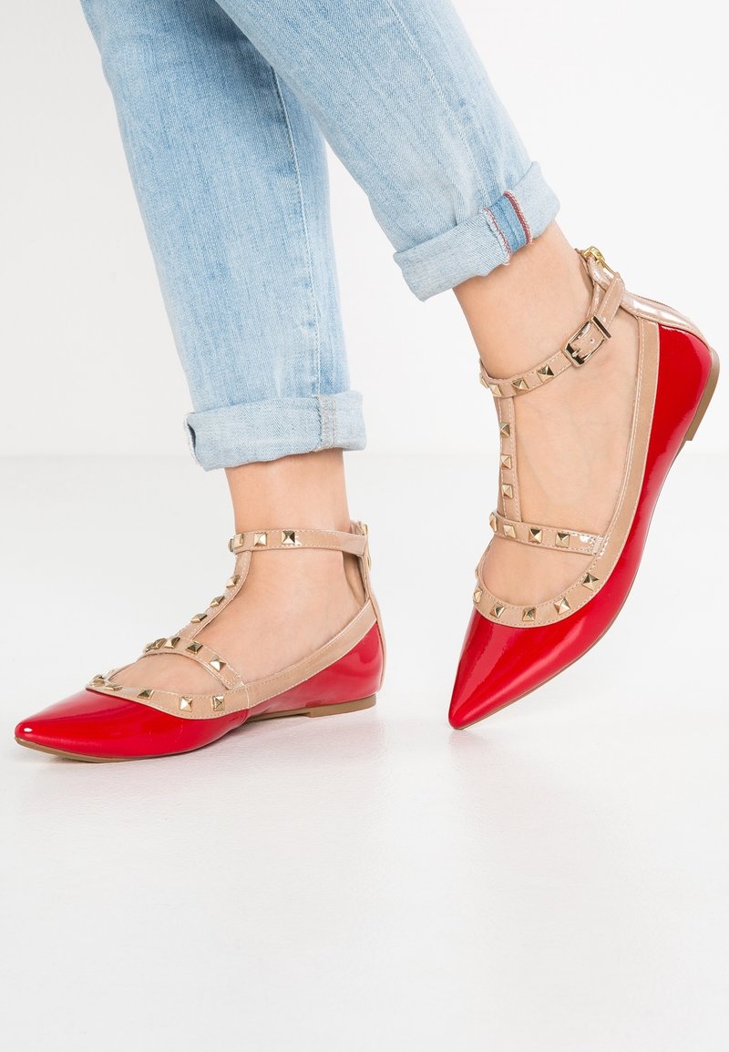 Ballerines en cuir verni rouge avec un bout pointu et des brides beiges transparentes ornées de clous dorés. Surface texturée avec une finition lisse.