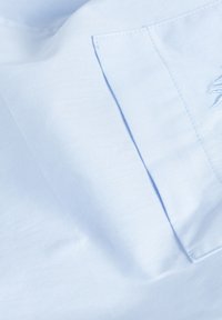 Jasnoniebieska tkanina o gładkiej fakturze ma naszywaną kieszeń. Na tkaninie znajdują się subtelne detale haftu, które wzbogacają jej wygląd.