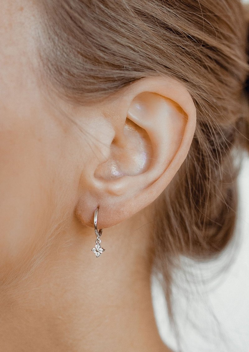 Orecchino a cerchio in argento con un piccolo design floreale che presenta tre pietre trasparenti, appeso a un sottile cerchio lucido.