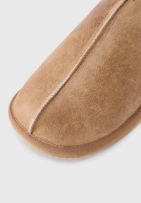 Pruun seemisnahast suss, millel on keskel õmmeldud õmblus ja kummist talla, näidatud suures plaanis valgel taustal.