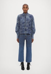 Denim shirt with floral pattern, blue tone, long sleeves, button-up design. Matching blue jeans with occasional patterned accents. Black ankle boots.
