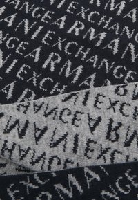 Tessuto lavorato a maglia con sezioni alternate di blu navy scuro e grigio chiaro, caratterizzato da schemi di testo in contrasto ripetuti in bianco e nero.