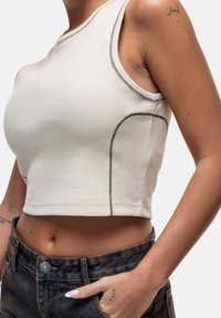 Top corto beige realizzato in tessuto a costine, con cuciture in contrasto nere lungo i bordi e un collo rotondo.