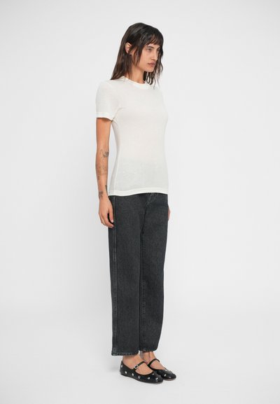 Tricou crem cu mânecă scurtă și decolteu rotund, asortat cu blugi închiși la culoare, cu talie înaltă, și pantofi Mary Jane negri cu accente argintii.