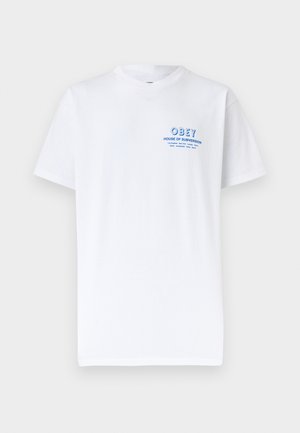 Tricou alb cu mâneci scurte și guler rotund, cu text mic albastru "OBEY HOUSE OF SUBVERSION" și nume de orașe pe partea superioară stângă a pieptului.