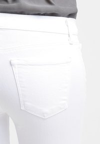 Jeans blancos con una textura suave, que cuentan con un bolsillo trasero. Los detalles de las costuras son visibles, con un corte recto en la cintura y un diseño minimalista.