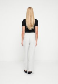 Szare szerokie spodnie z elastycznym paskiem, połączone z czarną bluzką z krótkim rękawem i czarnymi trampkami, widziane od tyłu.