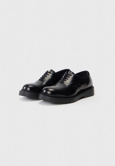 Schwarze Leder Schuhe mit glänzender Oberfläche, runder Zehenpartie und sechs Ösen-Schnürdesign. Sie verfügen über eine dicke Gummisohle mit strukturiertem Profil.