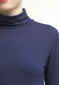 Námořnická roláková halenka vyrobená z měkké, elastické tkaniny s přiléhavým střihem, která má vysoký límec a hladkou texturu.