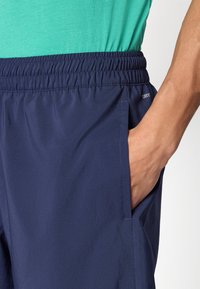 Σκούρο μπλε σορτς από ελαφρύ ύφασμα με ελαστική μέση, πλαϊνές τσέπες και λεία υφή. Περιλαμβάνει ετικέτα "DRY" κοντά στη μέση.