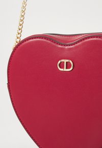 Red leather heart-shaped bag featuring a gold-tone hardware clasp and chain strap, with smooth texture and contrasting black edges.