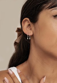 Boucles d'oreilles en argent en forme de cercle avec deux petites perles, présentées sur l'oreille d'un modèle sur un fond neutre. Les cheveux sont coiffés avec un ruban.