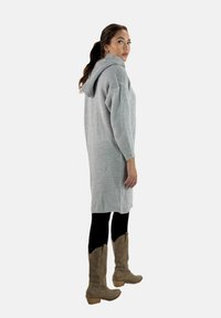 Strickkleid in Hellgrau mit Kapuze, lockerer Passform, gerippter Textur und langen Ärmeln; kombiniert mit beigen Cowboystiefeln.
