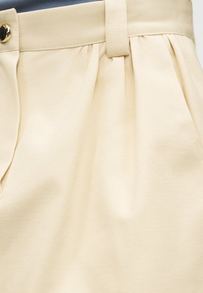 Κρεμ παντελόνι υψηλής μέσης με πτυχωτό μπροστινό μέρος, θηλιές ζώνης, πλαϊνές τσέπες και κλείσιμο με χρυσό κουμπί.