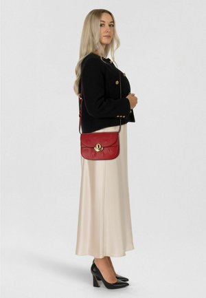 Borsa a tracolla in pelle rossa con motivo floreale in rilievo, accessori dorati e tracolla regolabile, abbinata a una giacca corta nera e un vestito color crema.