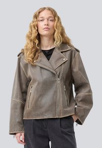 Brown leather biker jacket with silver zippers, snap buttons, and an oversized collar. Features a cropped cut and relaxed sleeves.