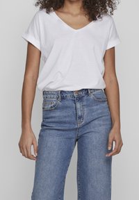 T-shirt blanc en V fabriqué en tissu doux, associé à un jean en denim bleu taille haute avec un design classique à cinq poches et une fermeture à bouton.