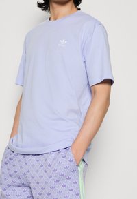 Světle fialové tričko s krátkým rukávem a kulatým výstřihem. Obsahuje malé bílé logo na hrudi a je vyrobeno z měkké bavlny.