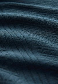 Țesătură texturată de culoare bleumarin cu un model geometric subtil, având o textură moale și netedă și o ușoară strălucire datorită reflecțiilor variate ale luminii.