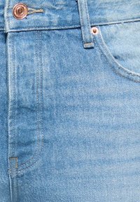 Šviesiai mėlynos spalvos džinsai iš džinso audinio su matomomis siūlėmis, penkių kišenių dizainu ir vario spalvos mygtuku bei kniedėmis. Audinio paviršius turi tekstūrą.