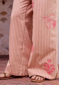 Pantaloni a gamba larga a righe in rosa e beige, con ricami floreali rosa sui lati, abbinati a sandali marroni piatti.