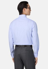 Šviesiai mėlyna dryžuota marškinėlių su apykakle, ilgomis rankovėmis ir glotnia tekstūra, derinami su tamsiai pilkais pritaikytais kelnėmis, turinčiomis galines kišenes.